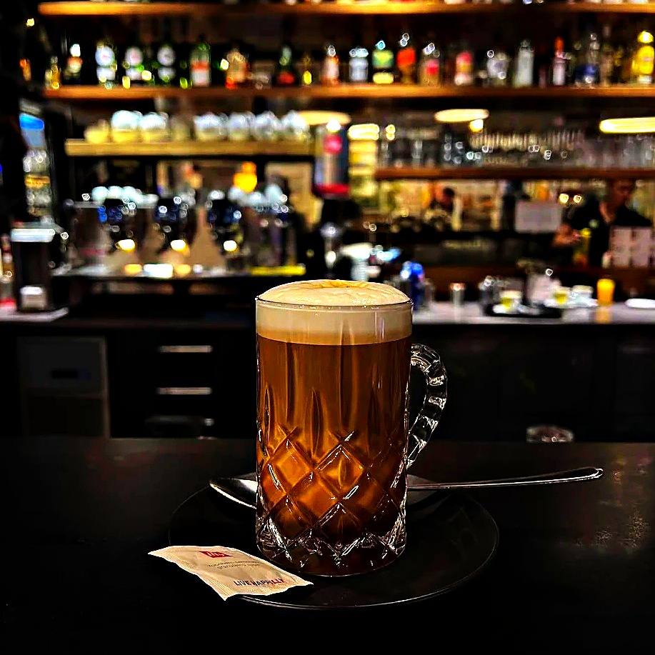 Caffè Caramello mit Milchschaum im geschliffenen Glas vor der Bar