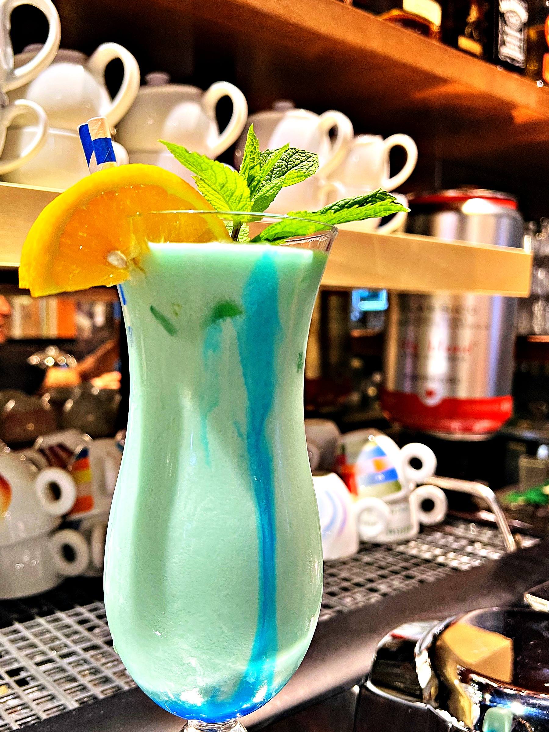 Hellblauer Cocktail mit Orangenscheibe und Minze im Hurricane-Glas