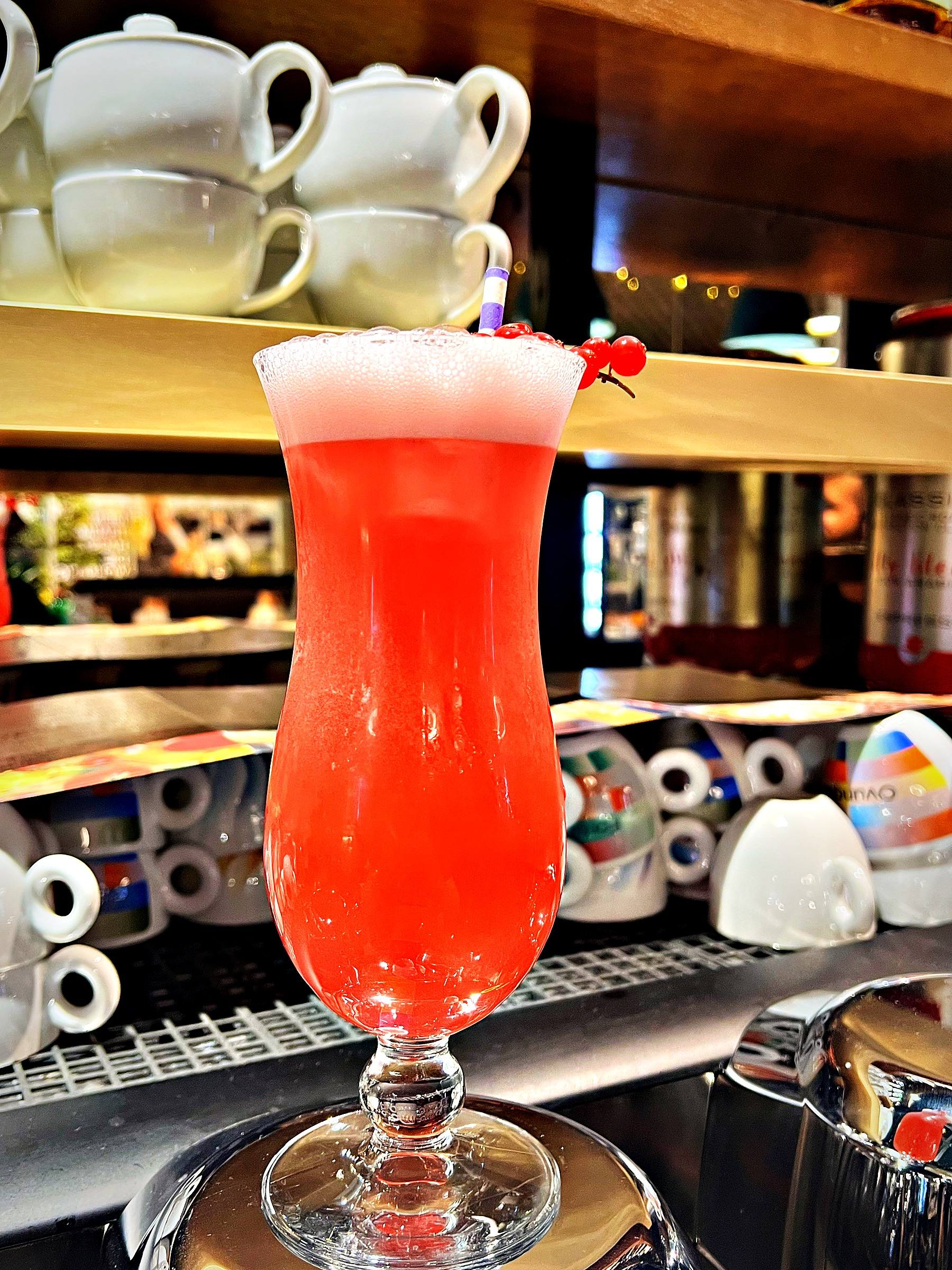 Pinker Cocktail mit Johannisbeeren im Hurricane-Glas an der Bar