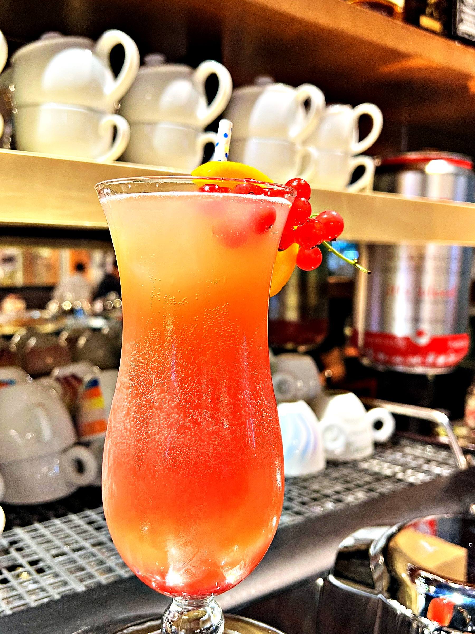 Roter Cocktail mit Orangenscheibe und Johannisbeeren im Hurricane-Glas an der Bar