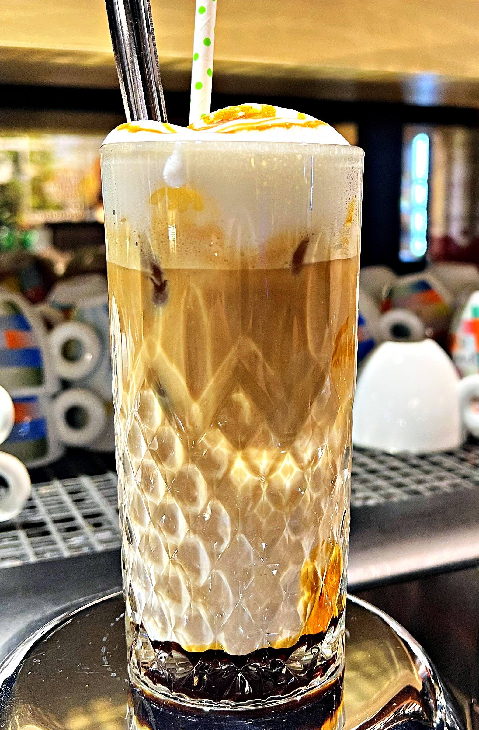 Kaffeegetränk im hohen Glas mit Milchschaum, Karamellsauce und Strohhalmen