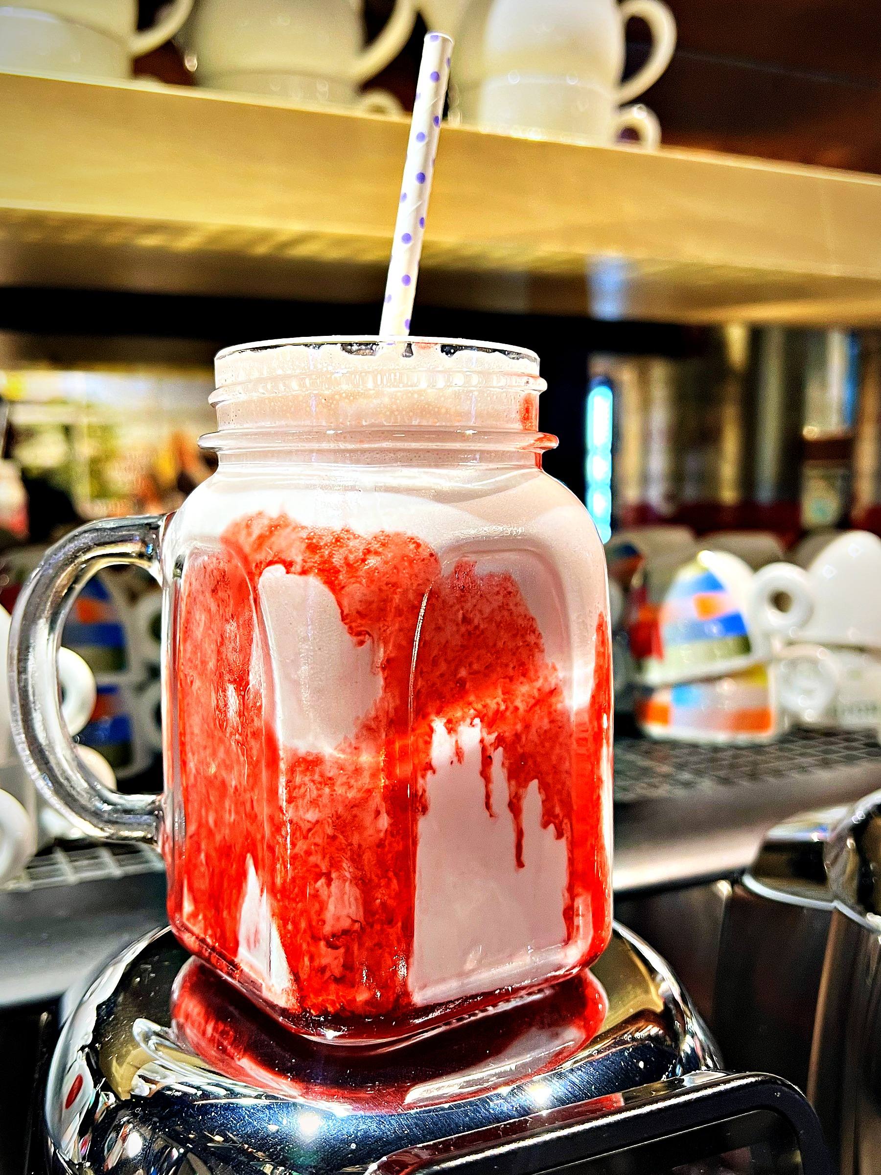 Erdbeer-Milchshake im Henkelglas mit roter Sauce und gestreiftem Strohhalm